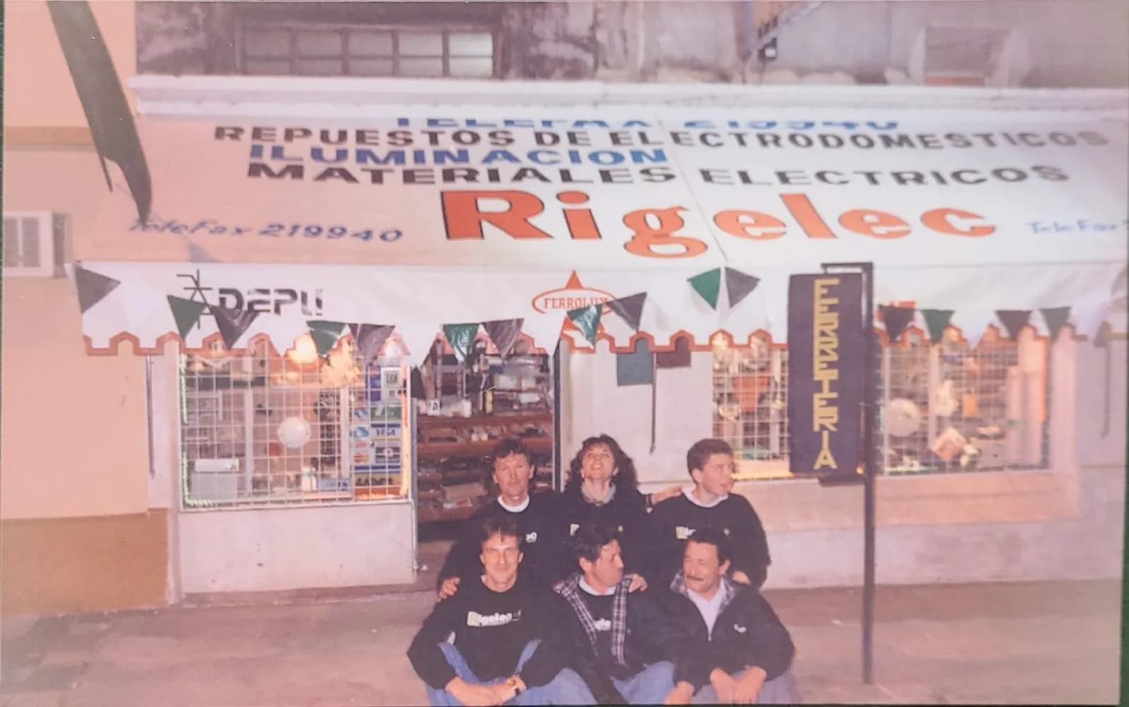 El equipo sentado en la vereda frente al local original de Rigelec, con el cartel de repuestos de electrodomésticos, iluminación y materiales eléctricos